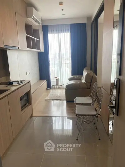 Modern living room with cozy sofa, sleek kitchen, and large window offering natural light.