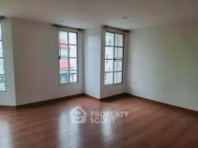 Spacious empty room with wooden flooring and large windows, perfect for customization.