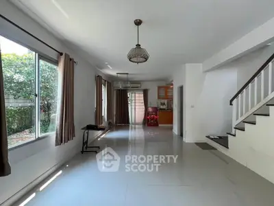 Spacious living room with large windows and modern staircase in a bright home.