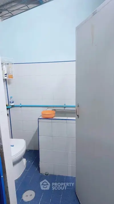 Compact bathroom with blue tiles and white fixtures, featuring a toilet and a small sink.