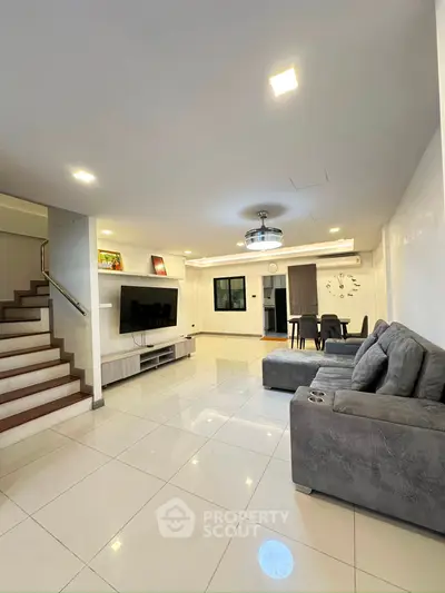Spacious modern living room with sleek design and elegant staircase, perfect for family gatherings.