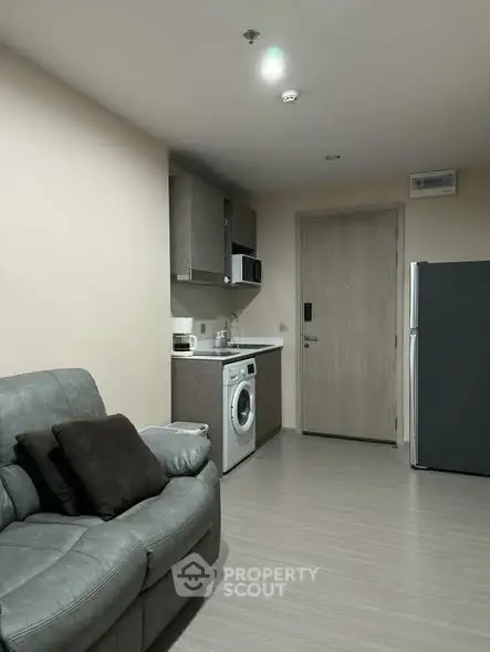 Modern apartment interior with cozy living area and compact kitchen featuring washing machine and fridge.