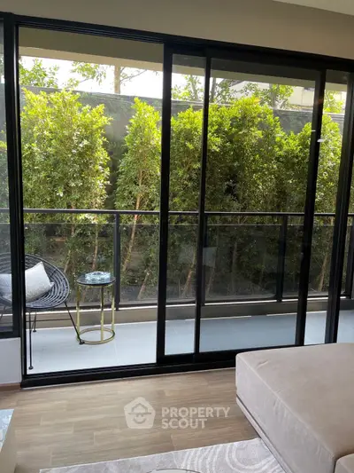 Modern living room with large glass doors opening to a lush balcony garden view.