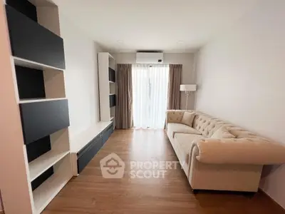 Spacious living room with elegant sofa and modern shelving, featuring natural light from large windows.