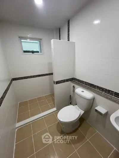 Modern bathroom with tiled floor and sleek fixtures, featuring a compact layout and natural light.