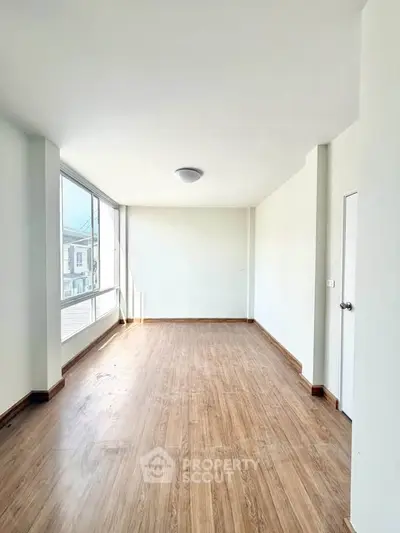 Spacious empty room with large windows and wooden flooring, perfect for customization.