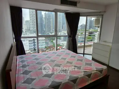 Spacious bedroom with city view and balcony access in modern high-rise apartment.