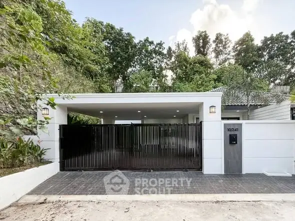 Modern gated entrance of a stylish residential property with lush greenery.