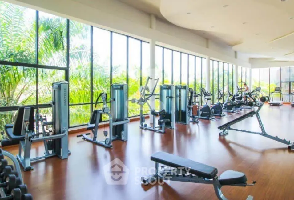 Spacious gym with modern equipment and large windows offering lush green views.