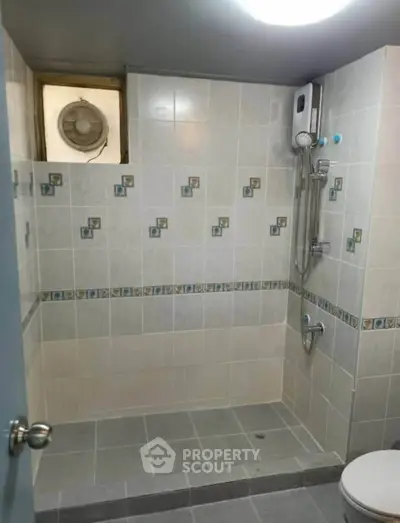 Compact bathroom with tiled walls and shower area, featuring a water heater and ventilation fan.