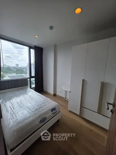 Modern bedroom with large window and stylish furniture in a high-rise apartment.