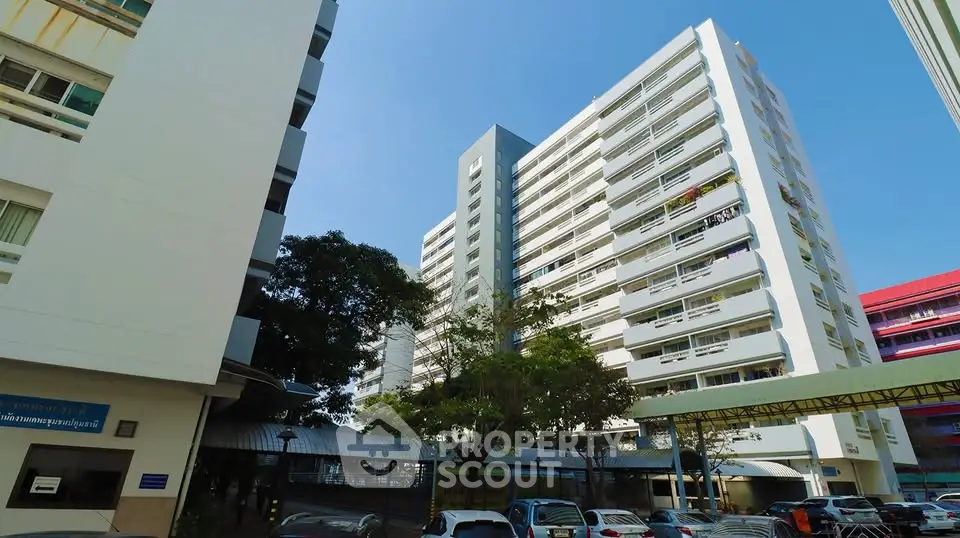 Modern high-rise residential building with parking area and clear blue sky.