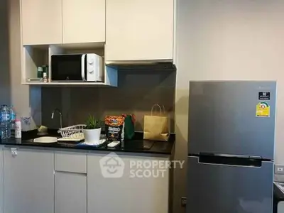 Modern kitchen with sleek cabinets, microwave, and stainless steel fridge, perfect for urban living.