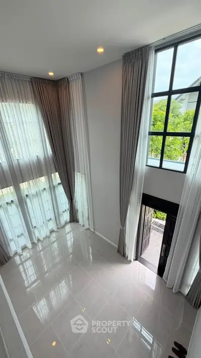 Stunning high-ceiling living room with large windows and elegant curtains, offering abundant natural light.