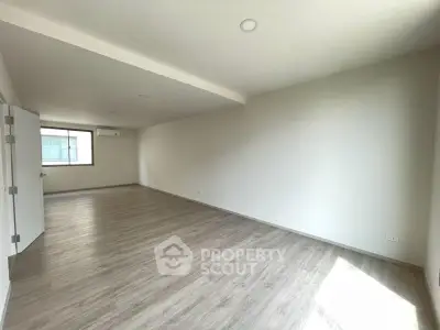 Spacious empty room with large window and wooden flooring, perfect for customization.