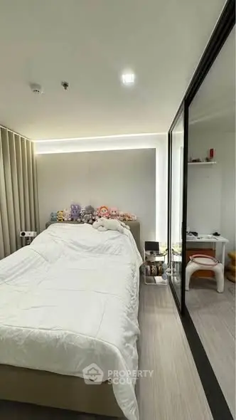 Cozy bedroom with plush toys and modern decor, featuring a mirrored wardrobe and sleek flooring.