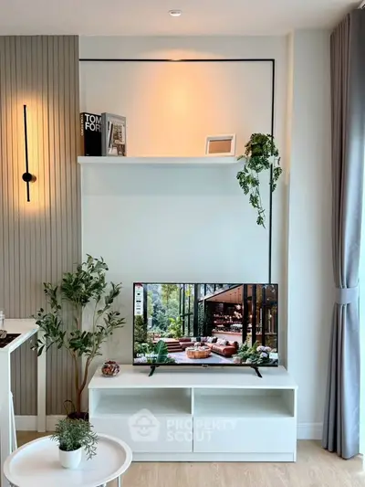 Modern living room with stylish decor and flat-screen TV, featuring elegant lighting and greenery accents.