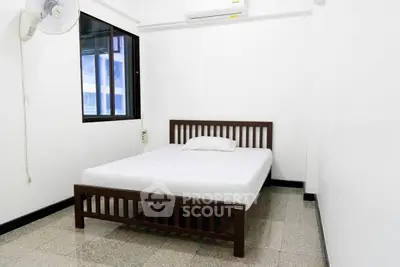 Minimalist bedroom with wooden bed frame and wall-mounted fan in bright apartment.