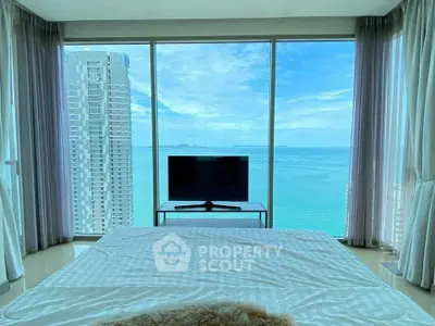 Luxurious bedroom with stunning ocean view through floor-to-ceiling windows in high-rise apartment.