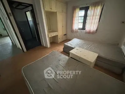 Spacious bedroom with twin mattresses and natural light, ideal for renovation.
