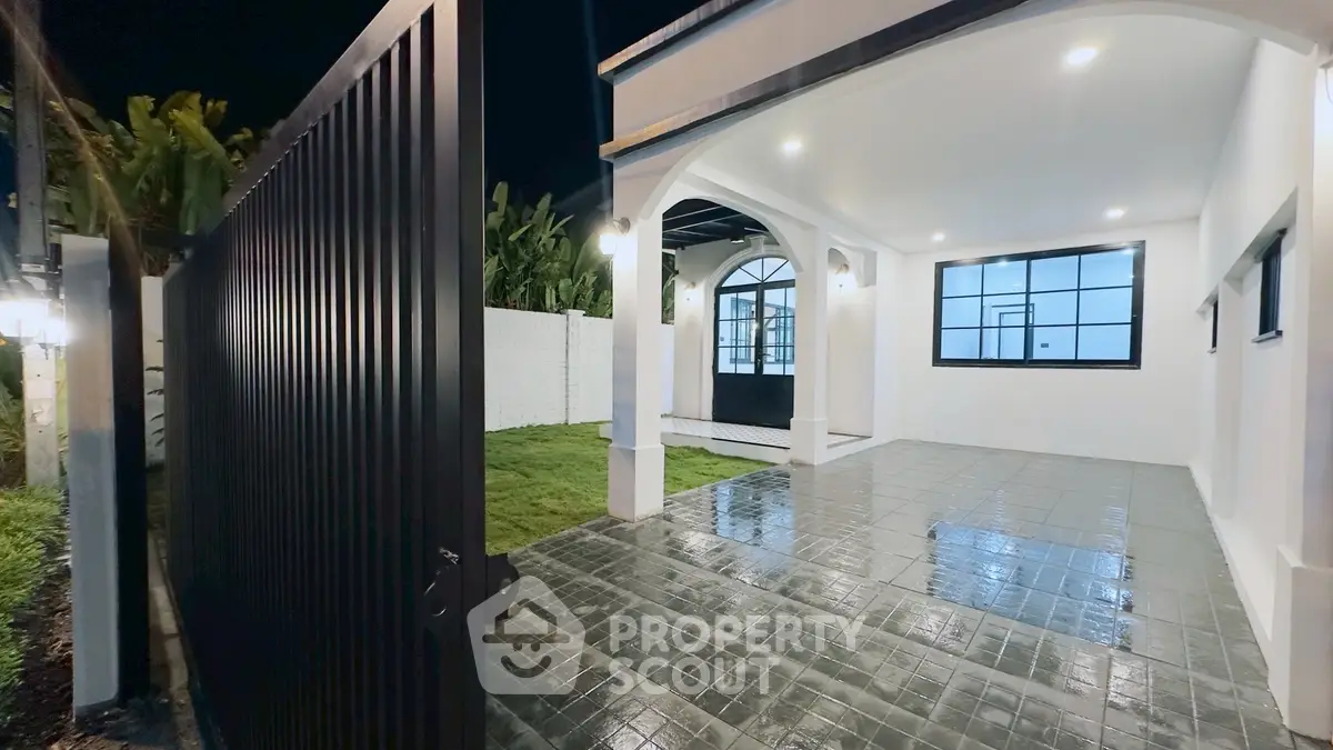 Elegant modern home entrance with spacious tiled patio and lush garden, perfect for evening relaxation.