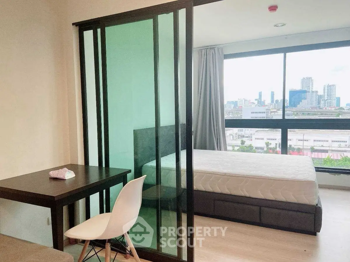 Modern studio apartment with glass partition and city view, featuring a cozy bedroom and work desk.
