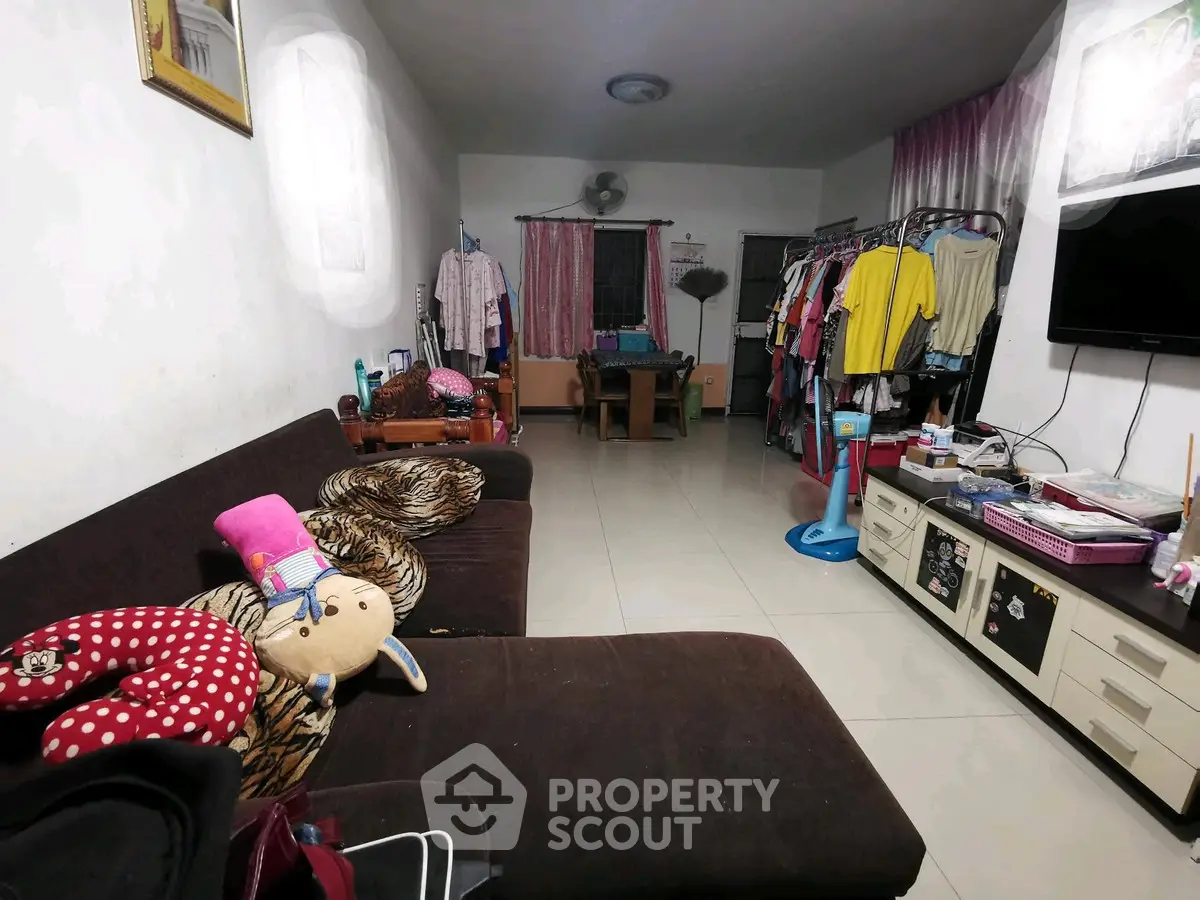 Cozy living room with brown sofa, TV, and clothes rack, ideal for small families or singles.