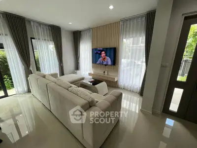 Modern living room with elegant sofa and wall-mounted TV, featuring large windows and stylish curtains.