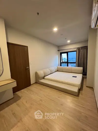 Spacious bedroom with large window and modern furnishings in a stylish apartment.