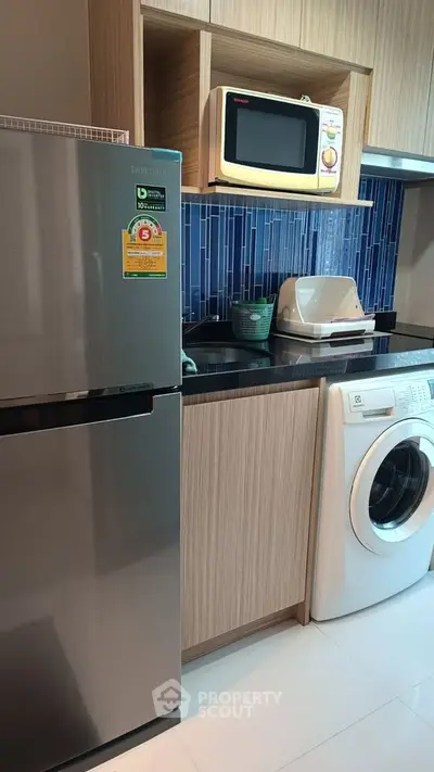 Modern kitchen with stainless steel fridge, microwave, and washing machine in sleek design.