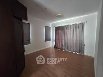 Spacious empty room with wooden flooring and large window with curtains