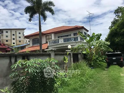 Charming two-story house with red tile roof and lush garden in tropical setting.