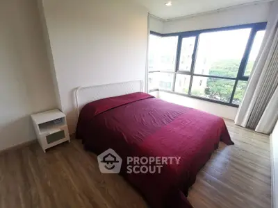 Spacious bedroom with large windows and elegant red bedding in modern apartment.