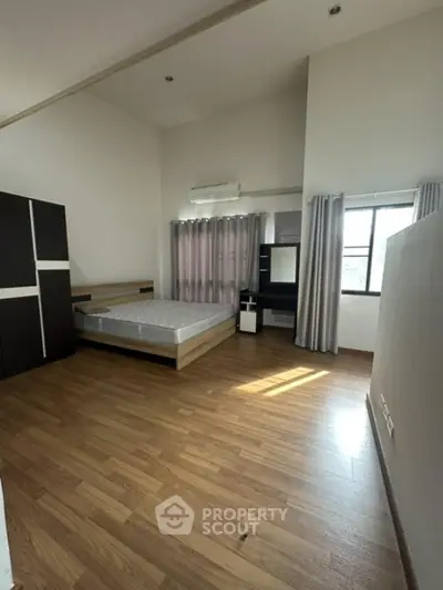 Spacious bedroom with wooden flooring and large windows for natural light