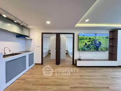 Modern open-plan living room with sleek kitchen and large TV, featuring wooden flooring and stylish cabinetry.