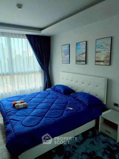 Modern bedroom with blue bedding, large window, and stylish decor in a contemporary apartment.