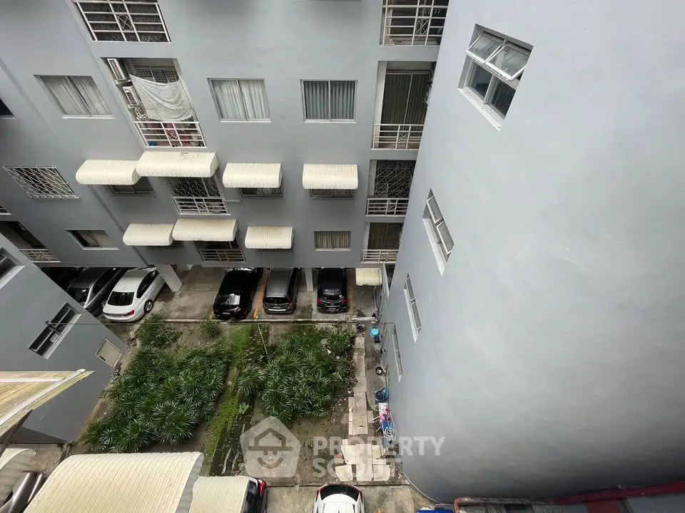 Aerial view of apartment building exterior with parking area and greenery.