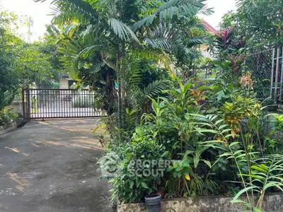 Charming garden entrance with lush greenery and gated driveway in a serene residential area.