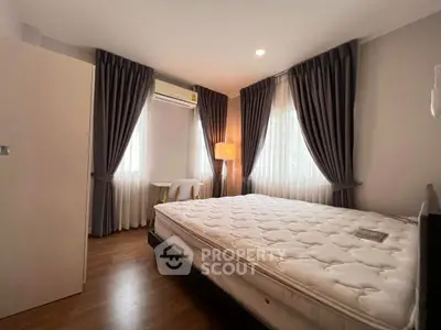 Cozy bedroom with large windows and elegant curtains, featuring a comfortable bed and ambient lighting.