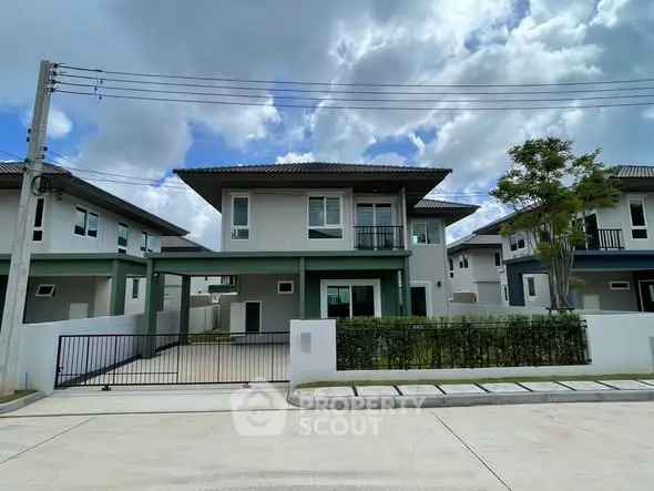 Modern two-story house with driveway and lush greenery under a cloudy sky.