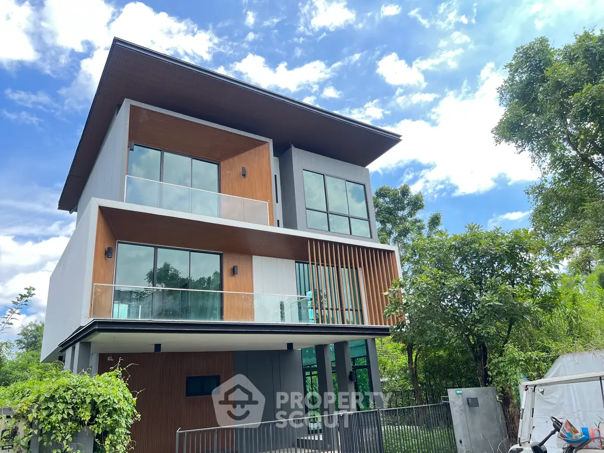 Modern three-story house with large windows and lush greenery