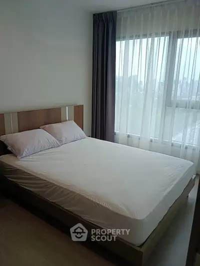 Modern bedroom with large window and city view, featuring a comfortable bed and elegant curtains.