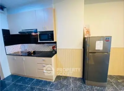 Modern kitchen with sleek cabinets, black countertops, and stainless steel fridge in a cozy apartment.