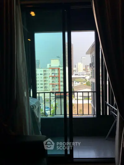 City view from a modern apartment balcony with sliding glass doors and curtains.