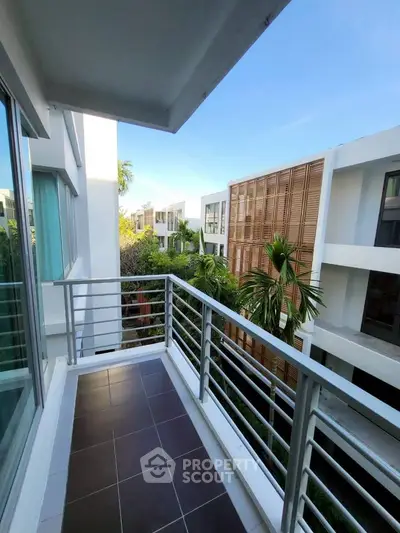 Modern balcony with sleek railing overlooking contemporary buildings and lush greenery.