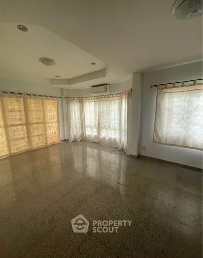Spacious sunlit living room with large windows and elegant ceiling design.