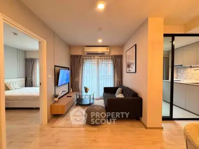 Modern living room with cozy sofa, wall-mounted TV, and open view to bedroom and kitchen.