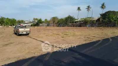 Spacious vacant land with potential for development, surrounded by lush greenery and clear skies.