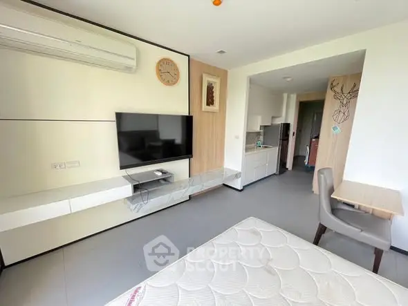 Modern studio apartment with sleek design, featuring a wall-mounted TV, air conditioning, and compact kitchen area.