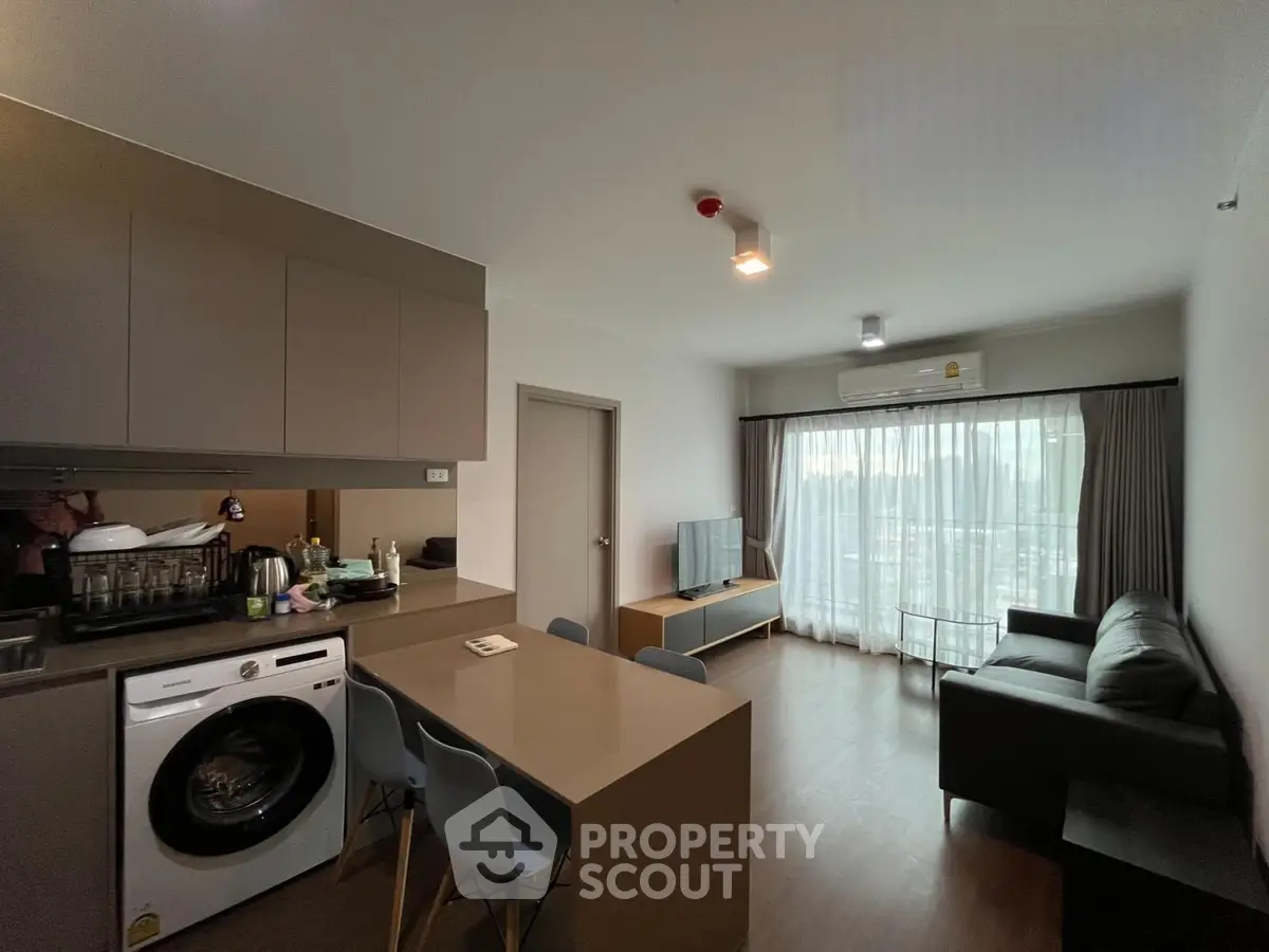 Modern open-layout living room with kitchen, featuring sleek furniture and natural light.